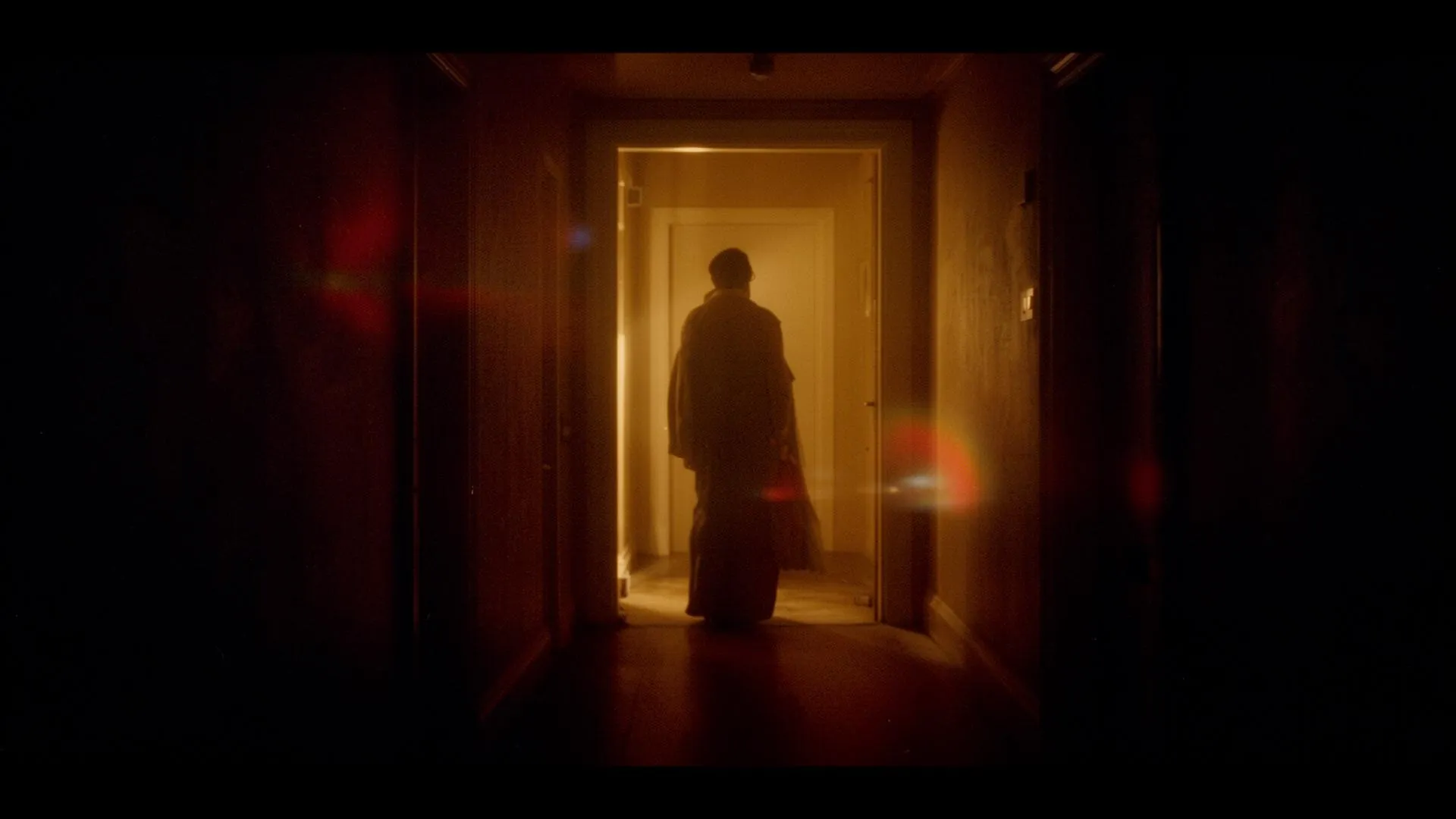 A lone figure framed in warm light at the end of a dark corridor